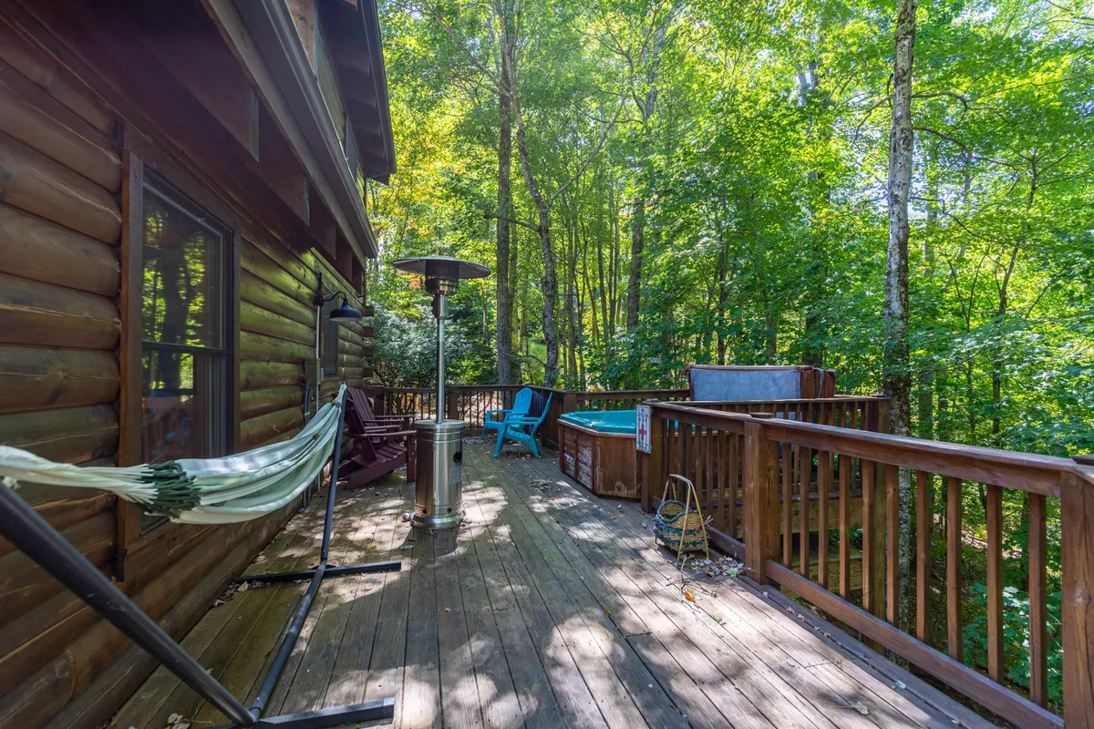 An inviting exterior deck featuring a hammock, a spacious hot tub, and comfortable outdoor seating, all surrounded by lush trees. The scene exudes tranquility and offers ample space for groups to gather, relax, and enjoy nature.