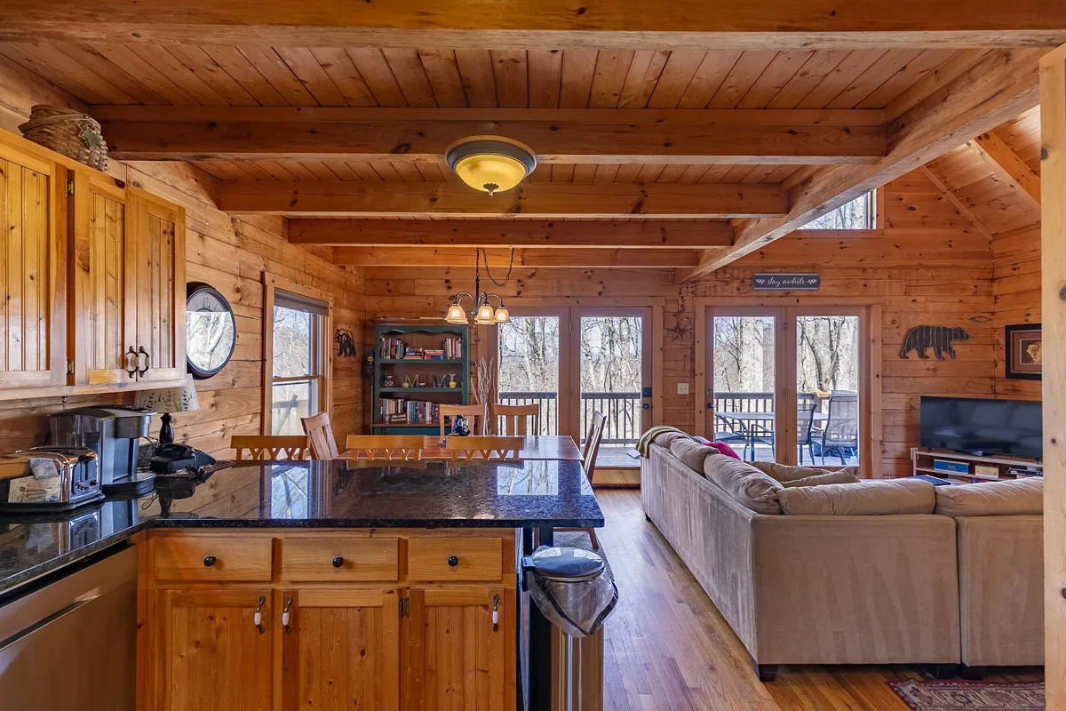 A wide-angle view that connects the kitchen, dining, and living spaces, showing a kitchen island, a cozy dining area, plush living room seating, and large windows leading to the deck. The light-filled, open layout is ideal for family gatherings, meals, and relaxed conversation.