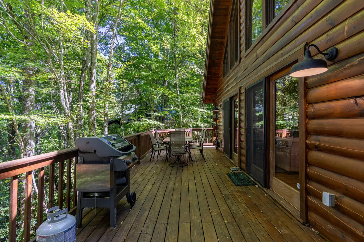 A welcoming wooden deck with an outdoor grill and seating, surrounded by lush trees. The area is set up for alfresco dining and provides a seamless transition between indoor comfort and outdoor fun.