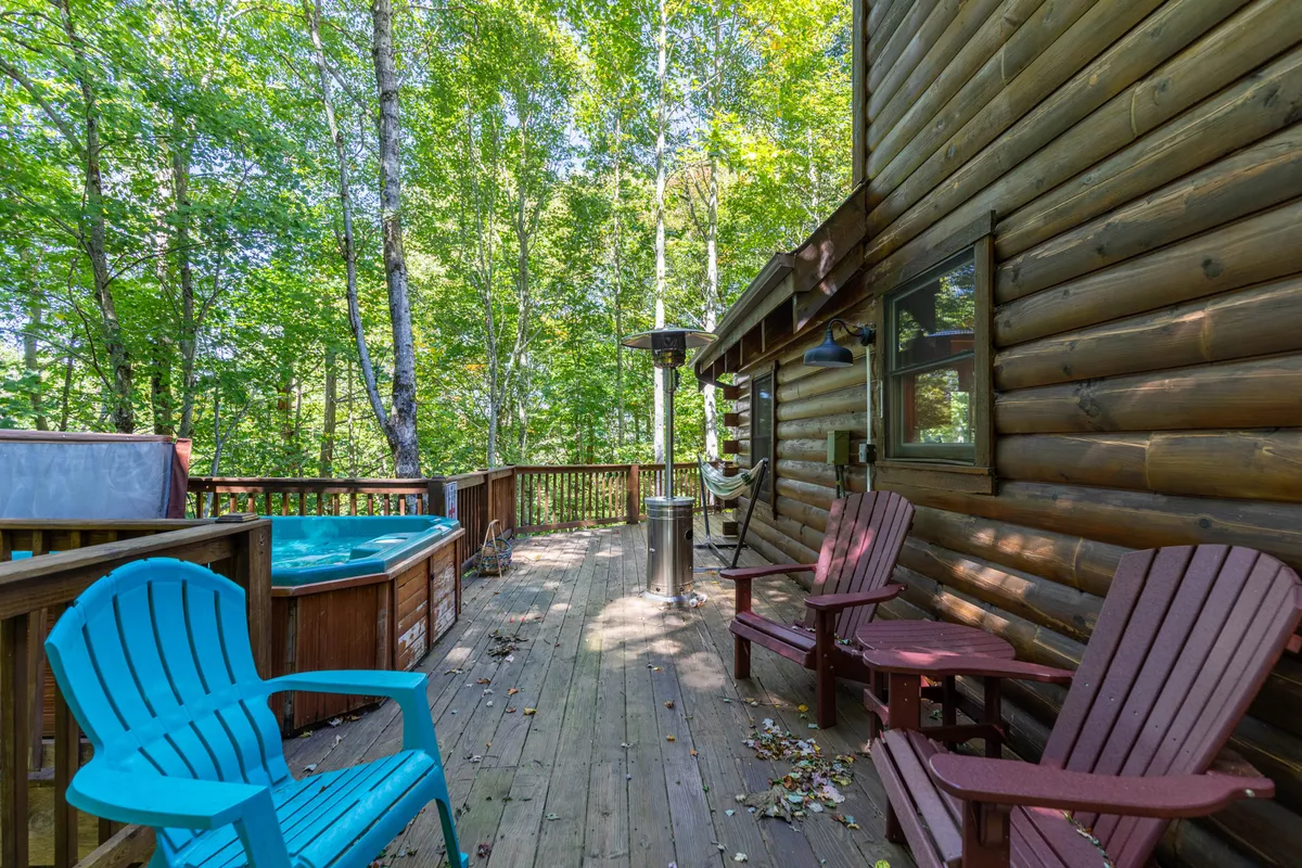 This exterior scene captures the inviting hot tub nestled on Mimi's Cottage's wooden deck, surrounded by lush trees. Blue and red Adirondack chairs sit nearby, perfect for relaxing with a book or socializing. The tranquil setting emphasizes a cozy and immersive nature experience, with the hot tub as a focal point for memorable evenings under the stars.