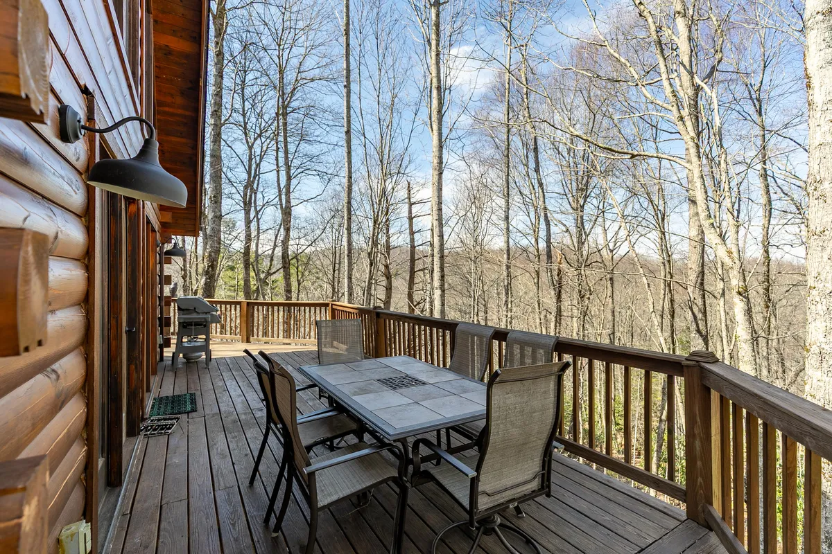 A peaceful deck scene showing a well-set outdoor dining table surrounded by trees, perfect for morning coffee or unwinding in nature. The area exudes tranquility and showcases the deck's multifunctionality beyond the hot tub and BBQ.