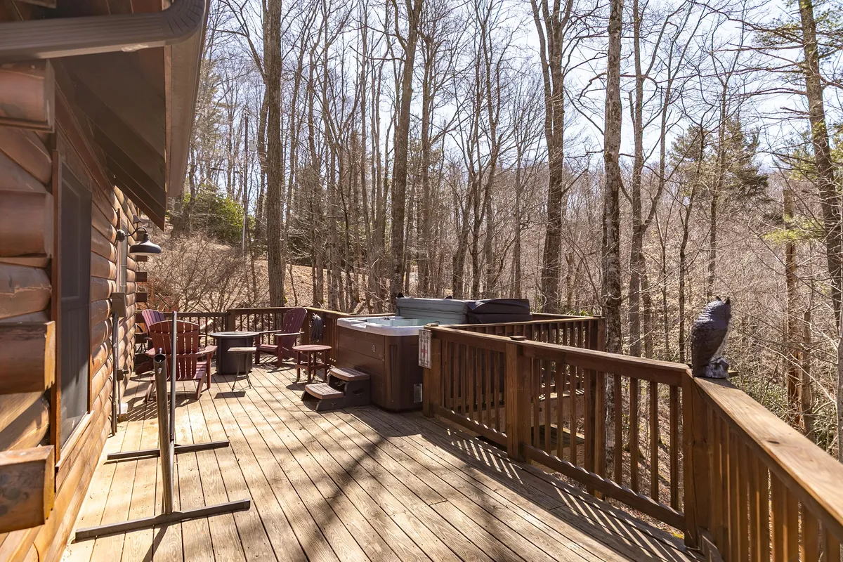 A peaceful deck scene with a bubbling hot tub, ample seating, and a backdrop of tall trees. The area invites guests to enjoy soaking, conversation, and stargazing in a private natural setting.