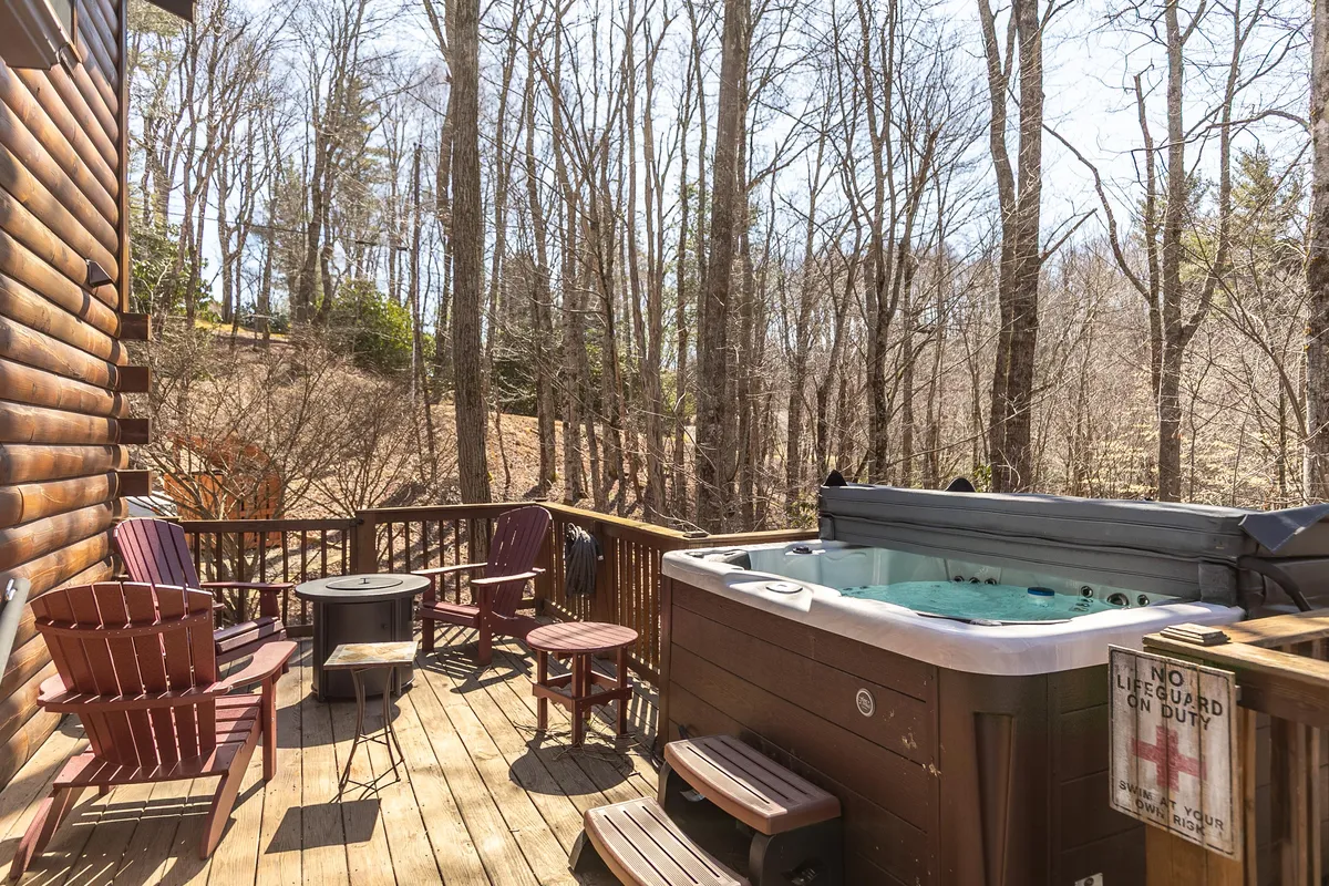 A view of the wooden deck with a bubbling hot tub and Adirondack chairs, surrounded by tall trees. The area is tranquil, ideal for unwinding after a day of hiking or exploring with your dog.
