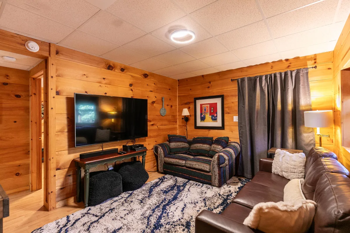 A welcoming living area featuring a comfortable sofa, a large television mounted on the wall, colorful artwork, and a soft rug. The setup invites guests to gather for movie nights or gaming sessions, with ample space for socializing and relaxing.