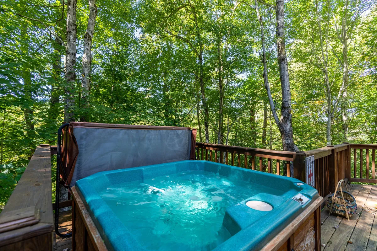 The photo spotlights a bubbling hot tub on a wooden deck, encircled by forested trees. The scene evokes relaxation and togetherness, with space for families to unwind after a day of activities.