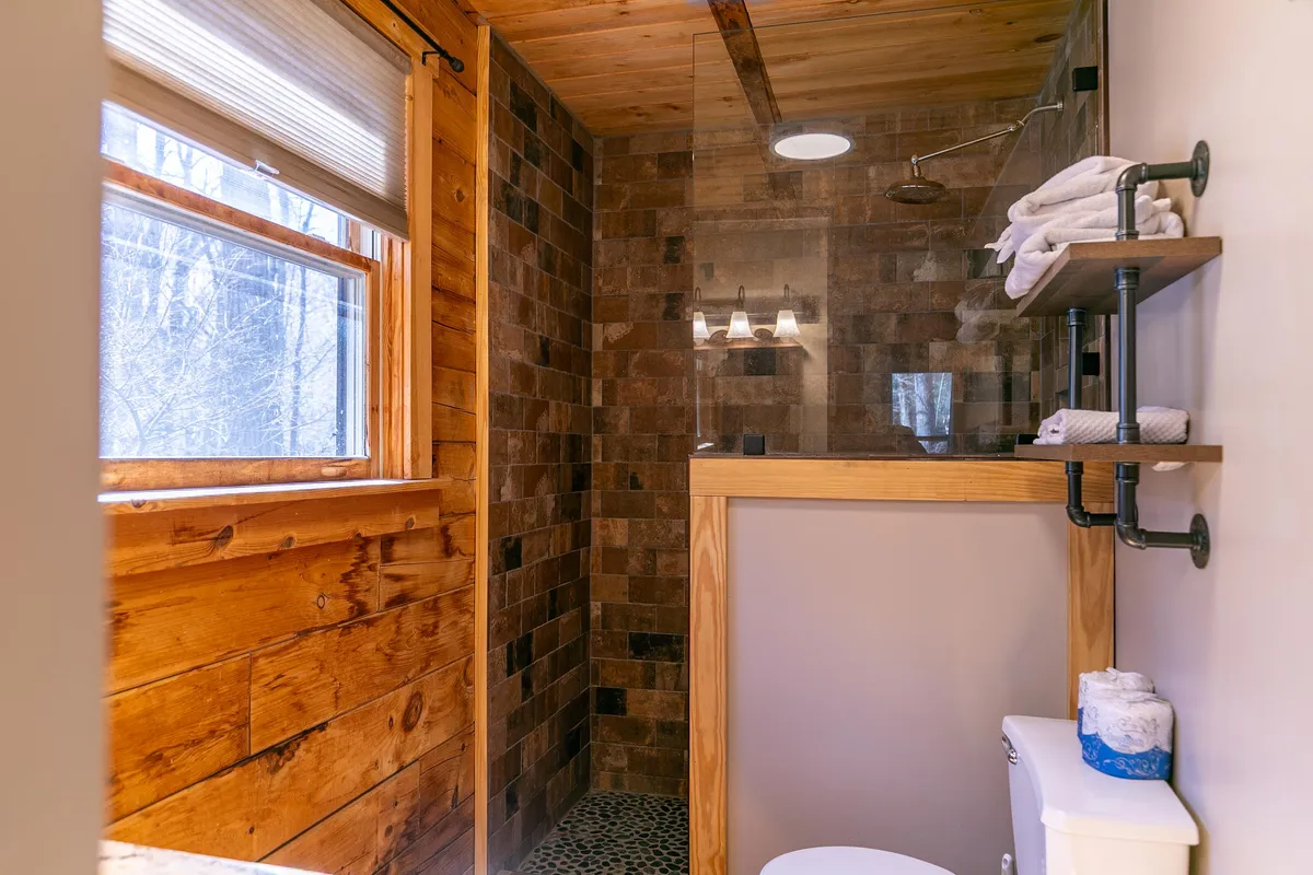 A bathroom featuring wooden accents, a glass walk-in shower enclosure, textured tile walls, and neatly arranged towels on shelves, evoking a serene, spa-like atmosphere.