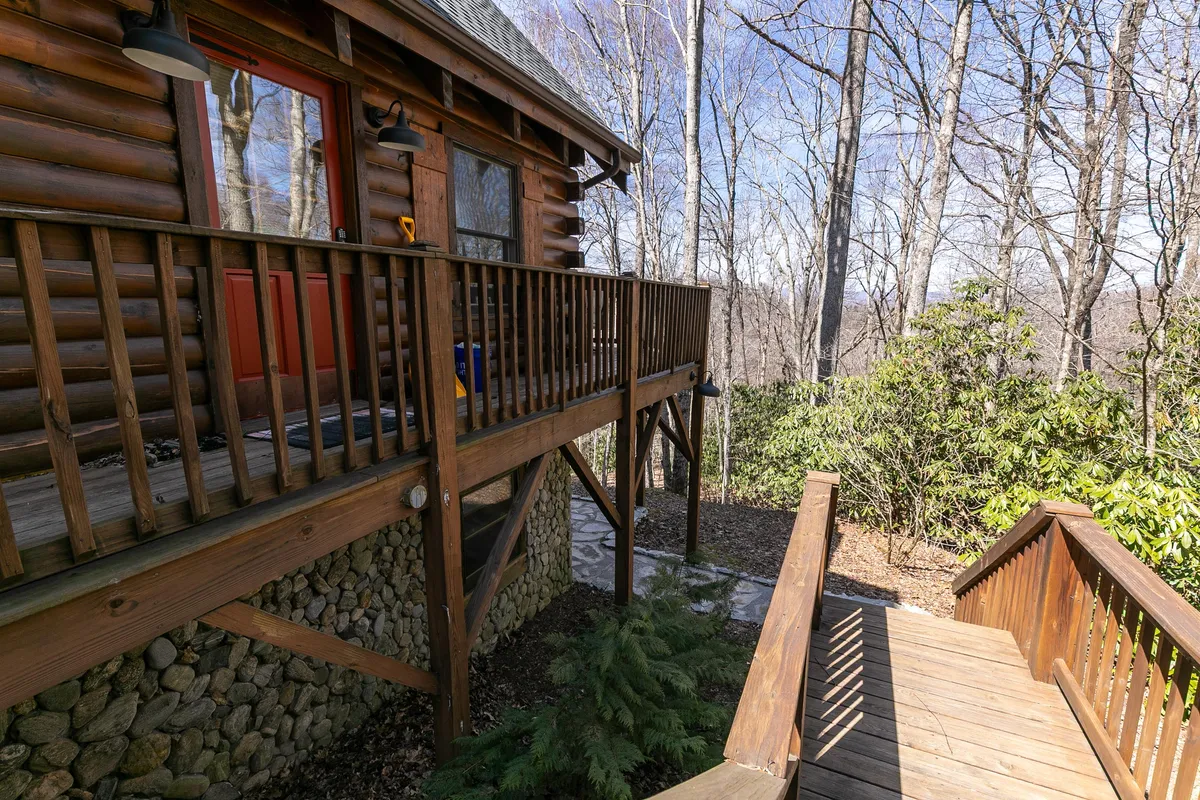 A picturesque view of the log cabin with a red door, wooden railing, and a winding pathway leading into the forest. The image highlights easy access to nature and nearby trails, emphasizing the adventure aspect for guests and their pets.